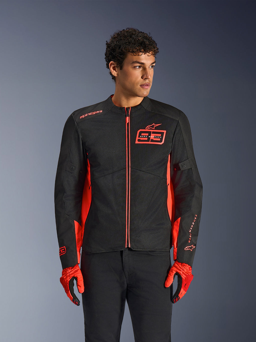 Alpinestars MM93 C-1 Air Jacket, urban motorjas, Red Fluo en zwart, gedragen door een model met bijpassende rode handschoenen en een zwarte broek, voorzien van een opvallend 93 Marc Marquez-logo op de borst en mesh-panelen voor optimale luchtstroom