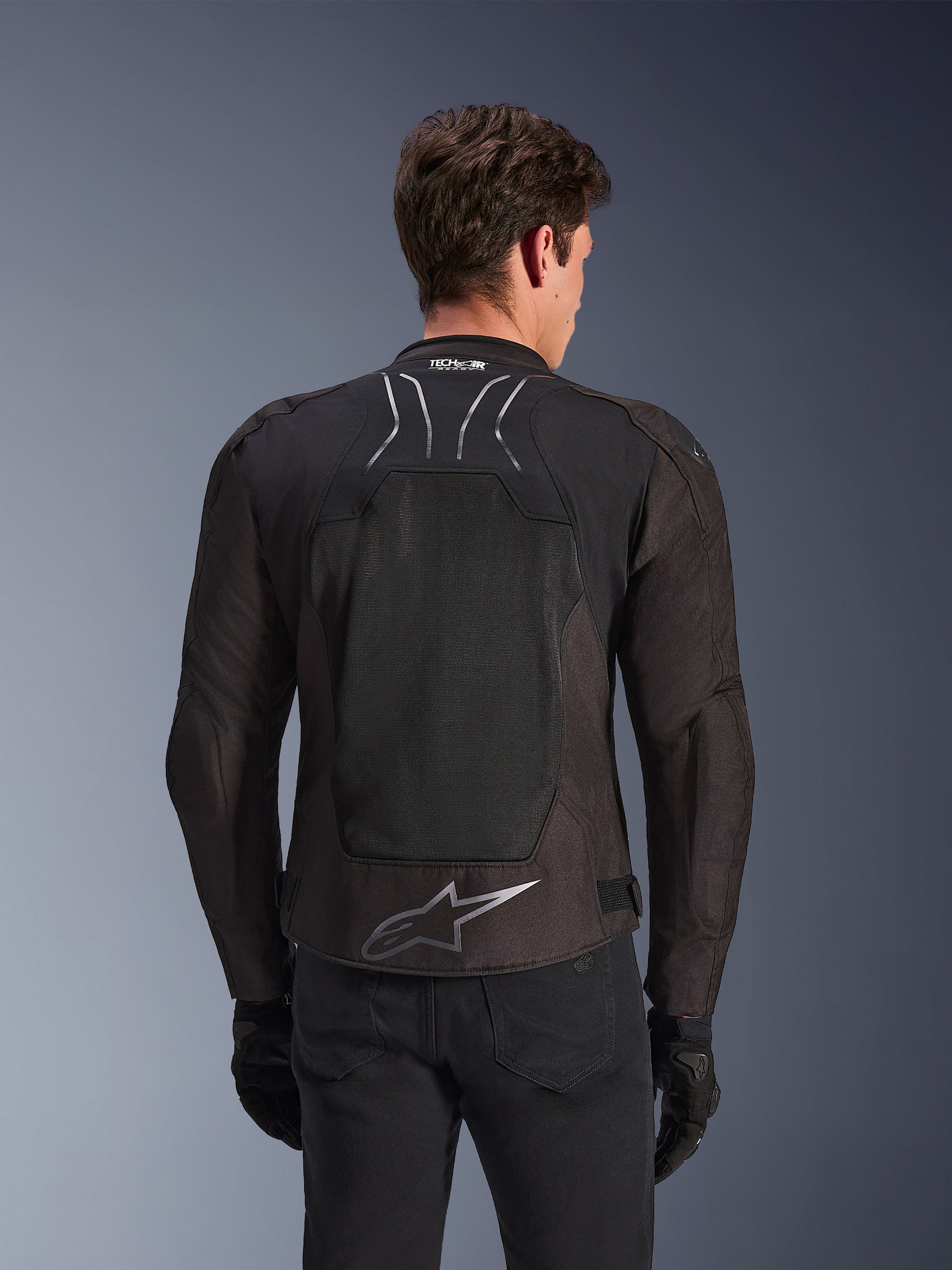 Alpinestars SMX Air Jas in Black Anthracite, achteraanzicht op een model, voorzien van een groot tech mesh rugpaneel voor ventilatie, Tech-Air Ready-branding op de kraag en een zilveren Astar-logo op de onderrug, gecombineerd met zwarte handschoenen en een motorbroek.