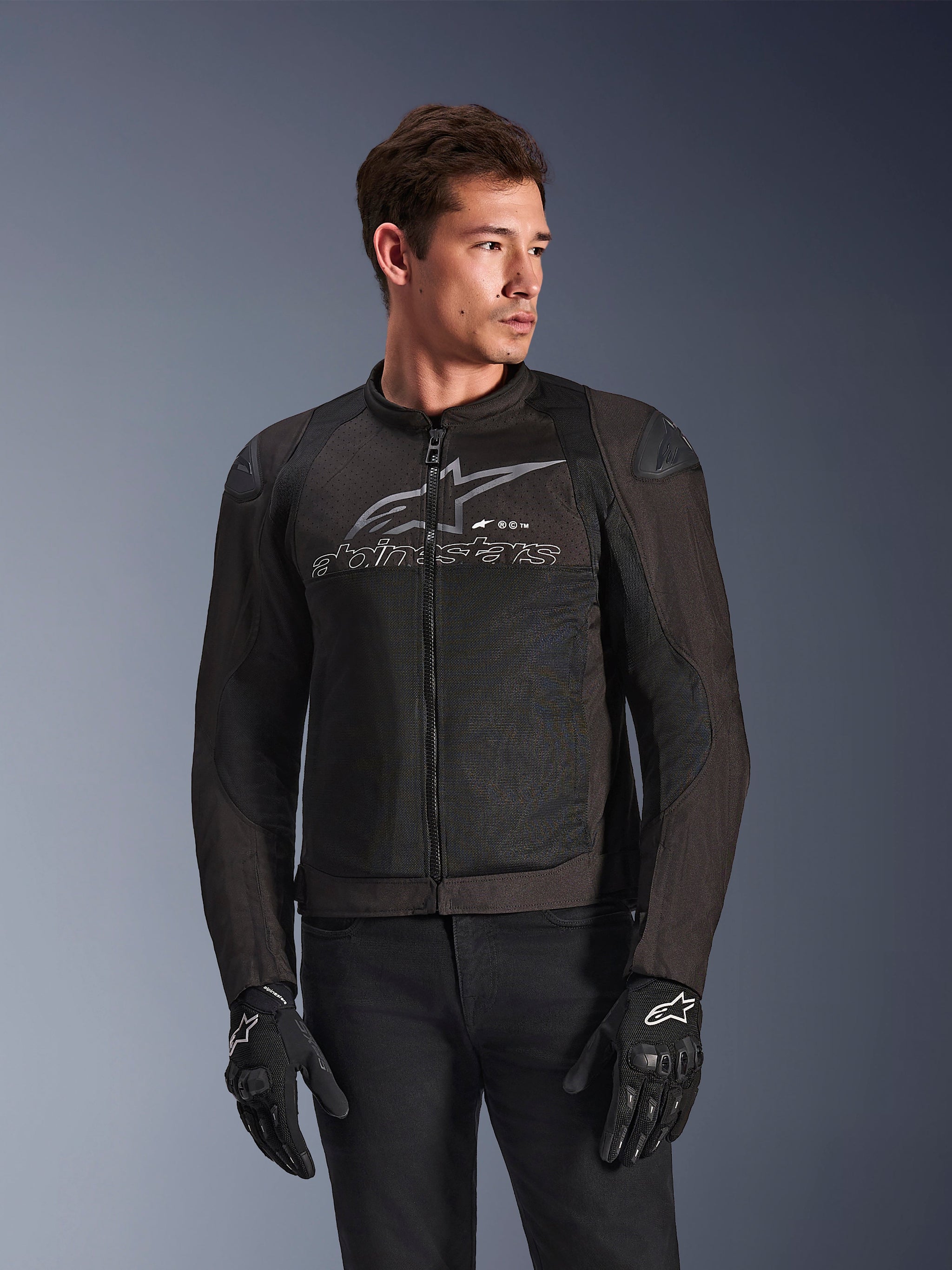 Alpinestars SMX Air Jacket in Black Anthracite, textiel motorjas met high-flow mesh panelen, groot grijs Alpinestars-logo en tekst op de borst, DFS Lite schoudersliders, gedragen door een model met zwarte motorhandschoenen, sportieve rijstijl