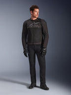 Male model wearing Alpinestars SMX Air Jacket, Black Anthracite motorcycle jacket with ventilated mesh panels and grey chest logo, paired with black pants and protective gloves, studio setting with a gradient background