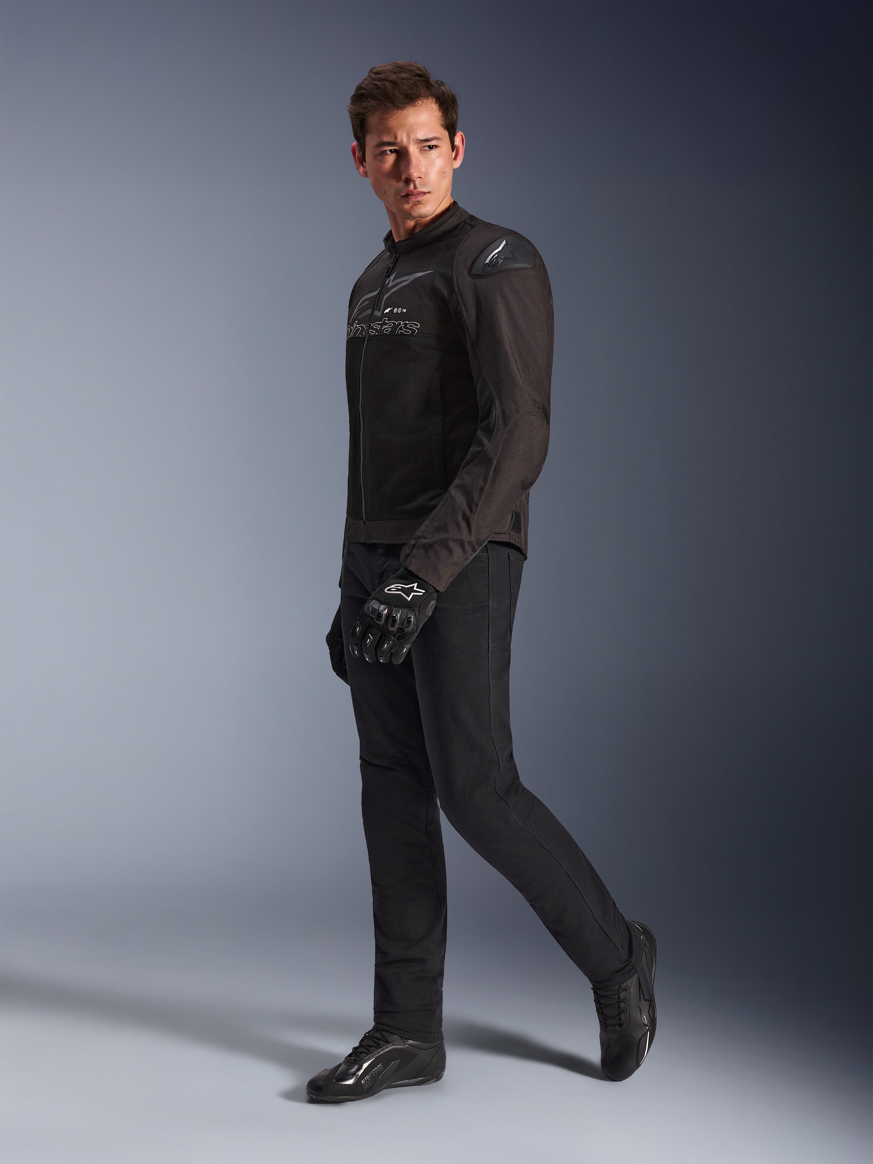 Alpinestars SMX Air Jacket in Black Anthracite, worn by model with matching black riding pants, gloves, and shoes, studio full-body shot, performance sport motorcycle gear featuring tech mesh and shoulder sliders