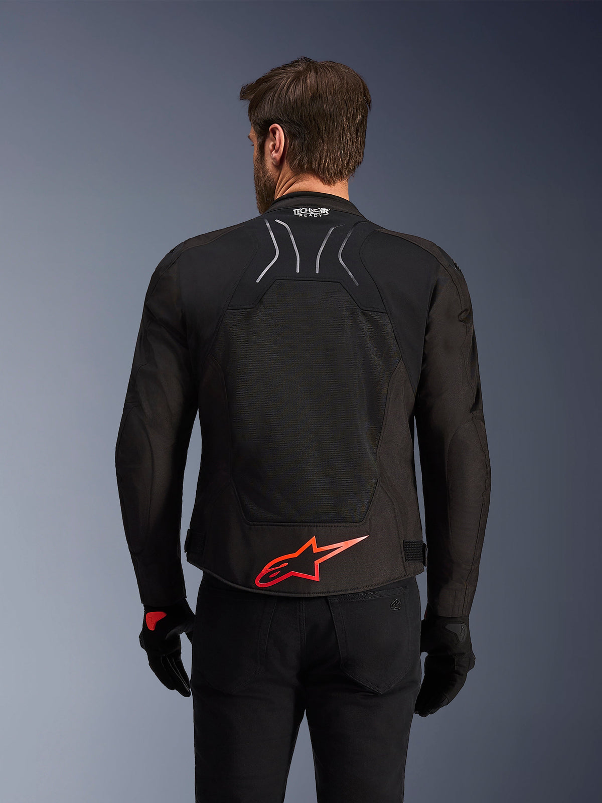 Alpinestars SMX Air Jacket, achteraanzicht, zwart met felrood Alpinestars-logo op de onderrug, voorzien van een technisch mesh-paneel voor een hoge luchtstroom en Tech-Air Ready-branding, gedragen door een mannelijke rijder met zwarte broek en handschoenen