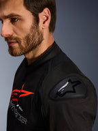 Alpinestars SMX Air Jacket, zwart en rood, close-up detail van de DFS Lite schouderbeschermer met sterlogo, gedragen door een man met een baard, textiele race- en sportmotorjas.