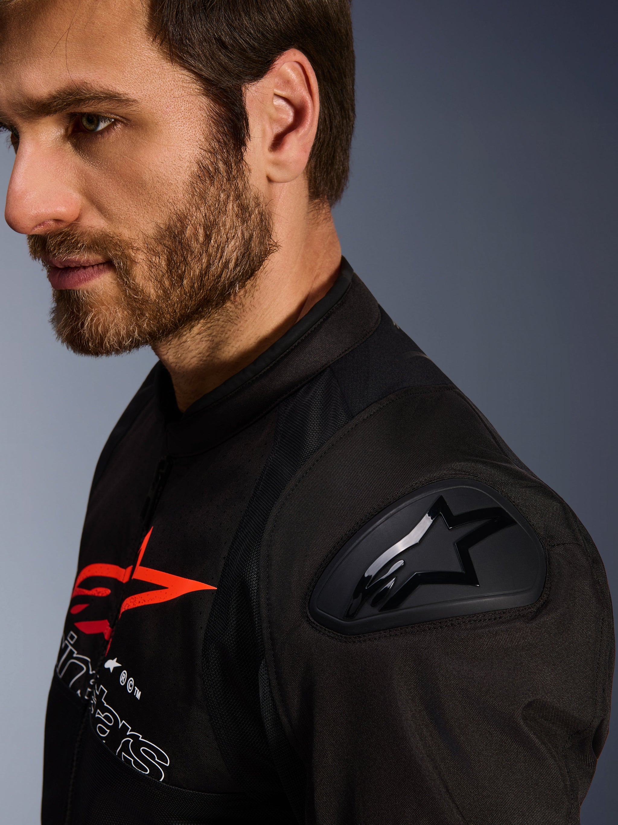 Alpinestars SMX Air Jacket, Black and Red, close-up detail of the DFS Lite shoulder protector with star logo, worn by a man with a beard, textile racing and sport motorcycle jacket.