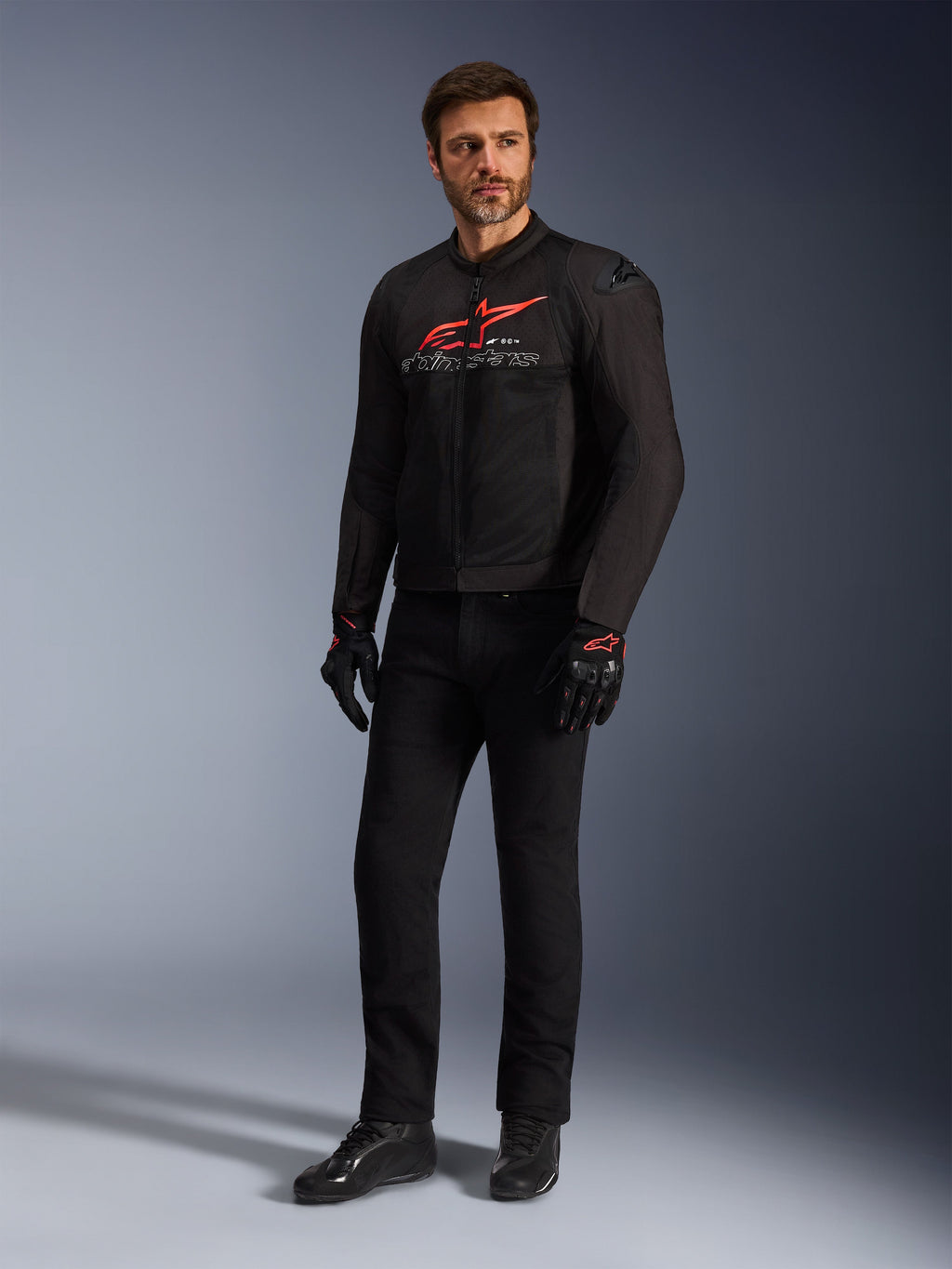 Mannelijk model draagt de Alpinestars SMX Air Jacket in Black Bright Red White, gecombineerd met een zwarte technische broek, zwart-rode handschoenen en zwarte motorschoenen, voorzien van een opvallend rood logo op de borst en witte merkdetails, volledige studio-opname van sportieve motoruitrusting.