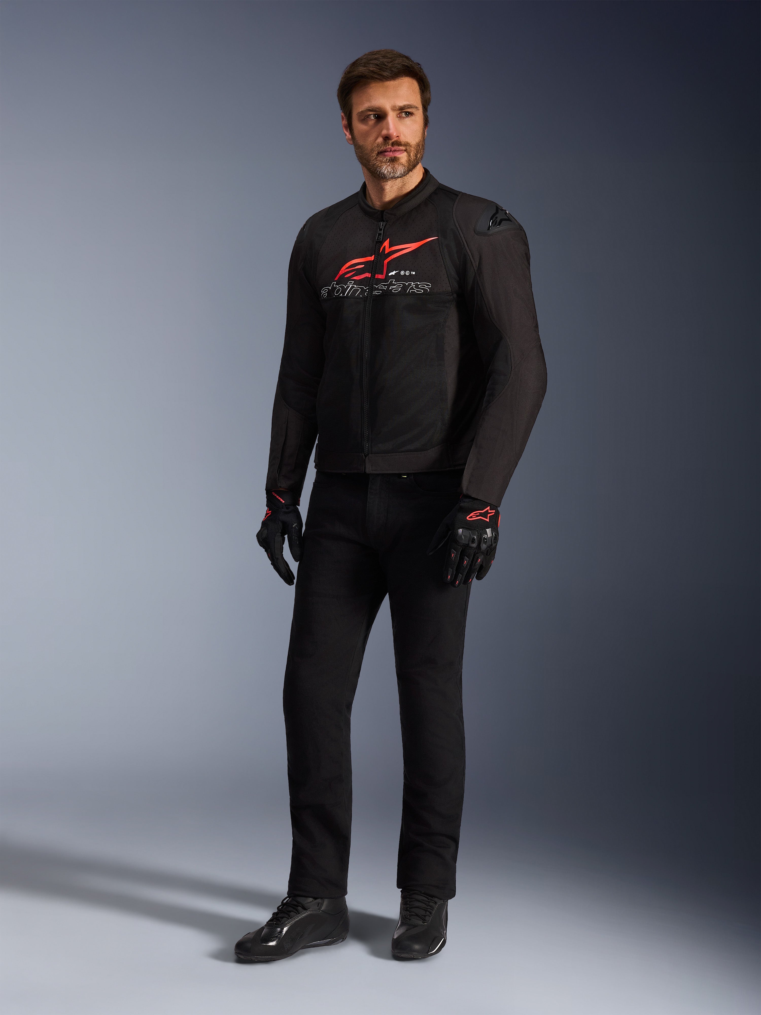 Mannelijk model draagt de Alpinestars SMX Air Jacket in Black Bright Red White, gecombineerd met een zwarte technische broek, zwart-rode handschoenen en zwarte motorschoenen, voorzien van een opvallend rood logo op de borst en witte merkdetails, volledige studio-opname van sportieve motoruitrusting.