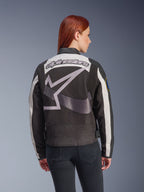 Alpinestars Idles damesjas, zwart en gebroken wit, achteraanzicht met een groot grijs sterlogo en Alpinestars-woordmerk, gedragen door een roodharig model, vintage-geïnspireerde urban motorjas met accordeonpanelen.