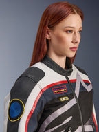 Alpinestars Idles damesjas, Off White, vlamrood en zwart, met vintage-geïnspireerde race-patches en een rondom lopend logo, constructie van textiel en leer, urban motorstijl gedragen door een model.