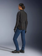 Vrouw draagt de Alpinestars Stella Aeroshell Airflow jas, Black Anthracite, driekwart achteraanzicht met ademende mesh-panelen en een verlengd achterprofiel, gecombineerd met een blauwe denim motorjeans en zwarte Alpinestars-schoenen