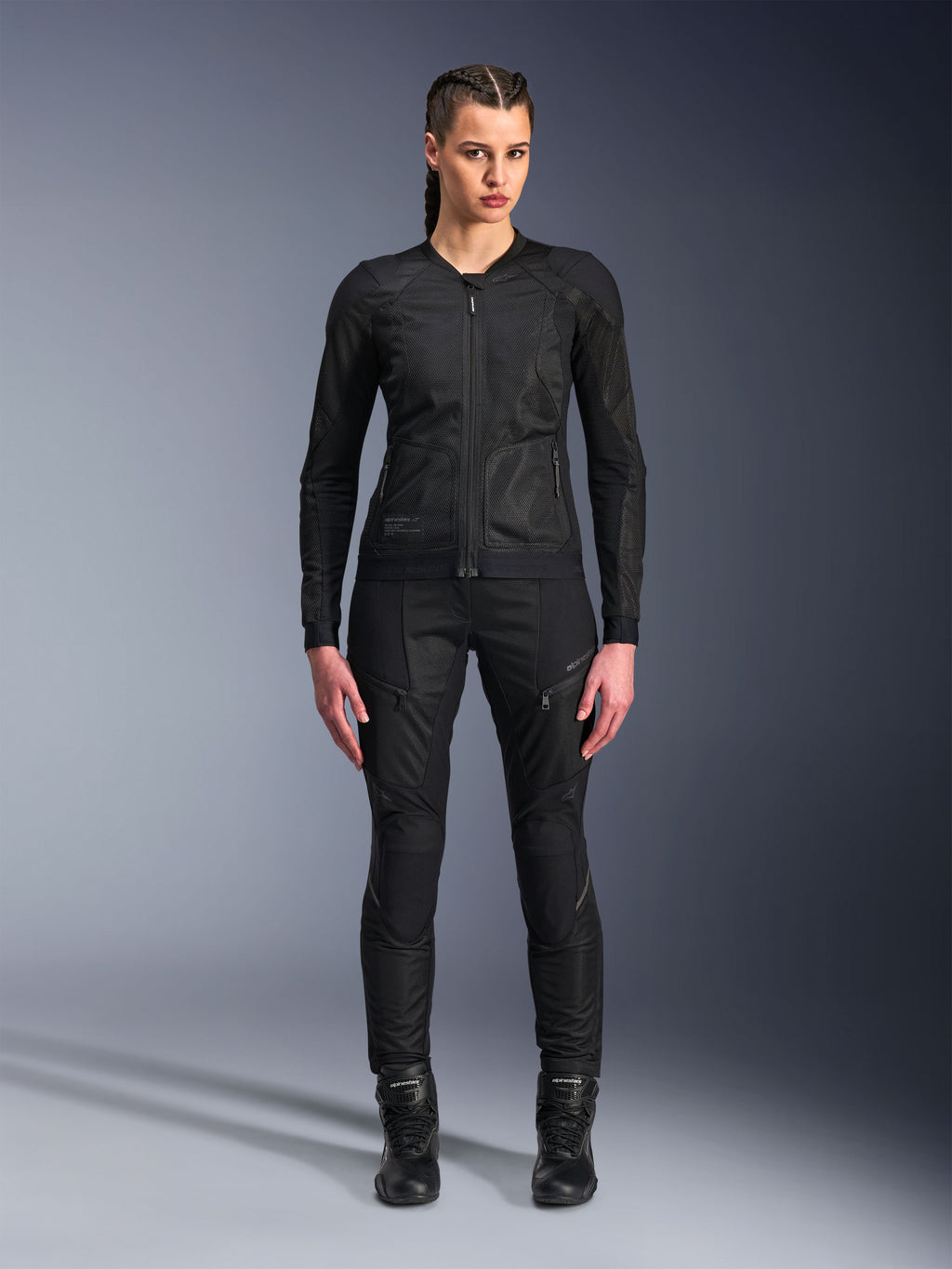 Alpinestars Stella Troop-Air jas, motorjas voor dames, zwart, technische 2D-mesh constructie met een minimalistisch ontwerp, gedragen met een zwarte motorbroek en motorlaarzen, hedendaagse stedelijke motorstijl.