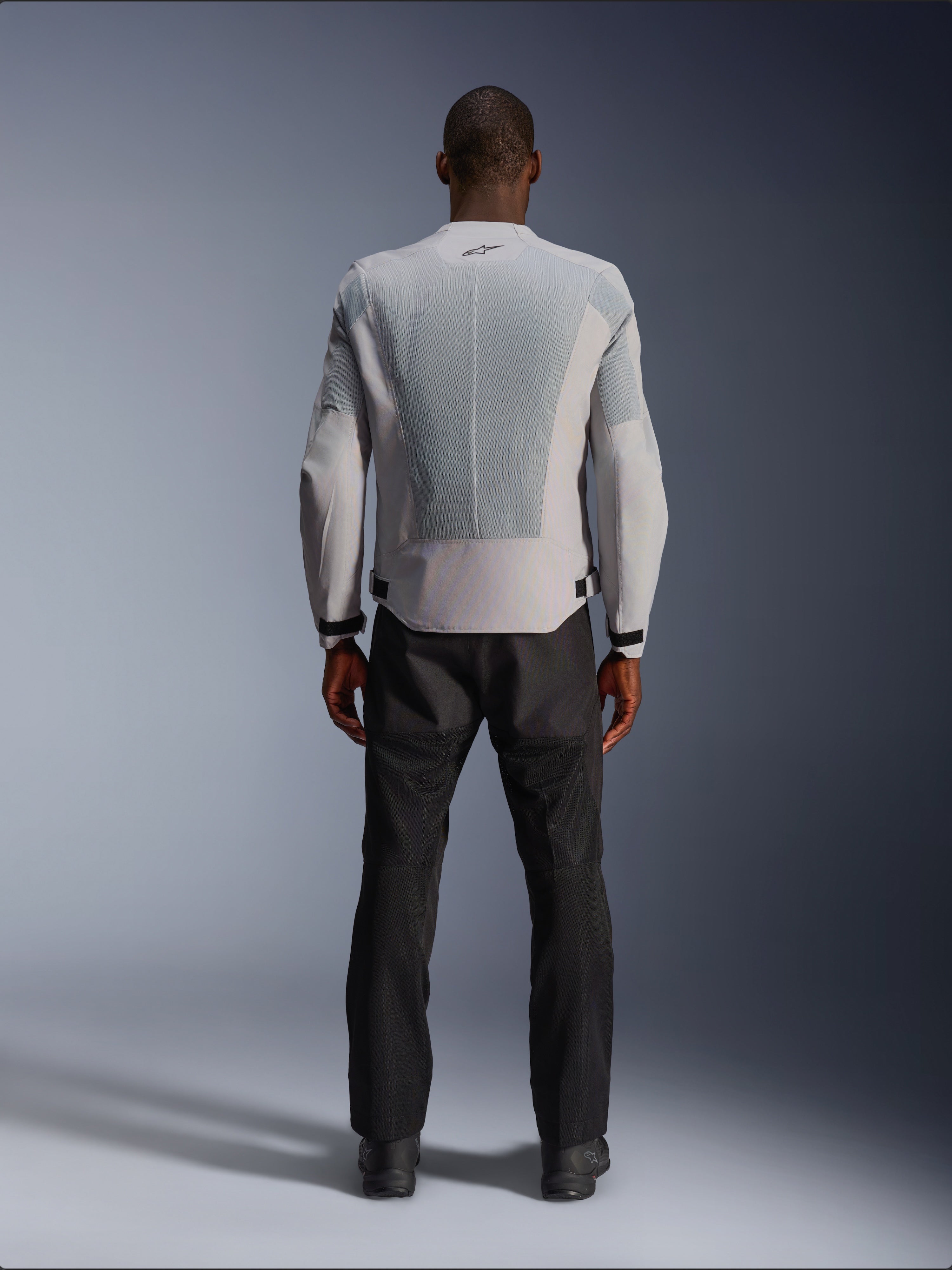 Alpinestars C-1 Air Jacket in Silver, vanaf de achterkant gezien op een mannelijk model, textiele motorjas met grote tech mesh ventilatiepanelen, klein zwart logo in de nek en tailleverstellers, gedragen met een zwarte motorbroek voor een urban contemporary look.
