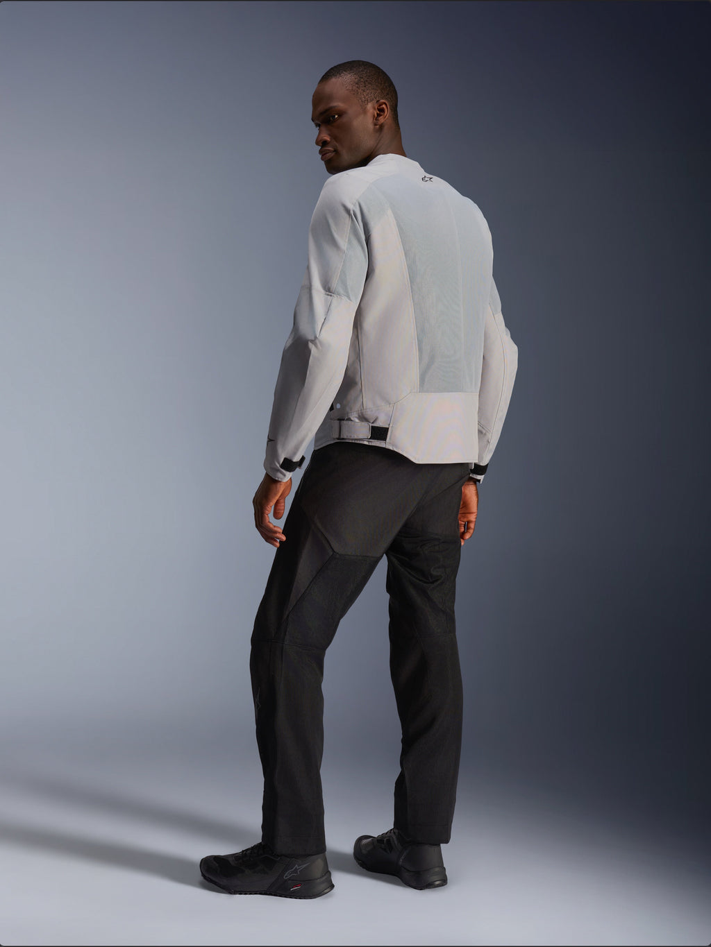 Alpinestars C-1 Air Jacket, zilver en grijs, van achteren bekeken op een model, voorzien van geventileerde tech mesh-panelen en reflecterende logo's, gedragen met een zwarte broek en schoenen, urban contemporary motorkleding.