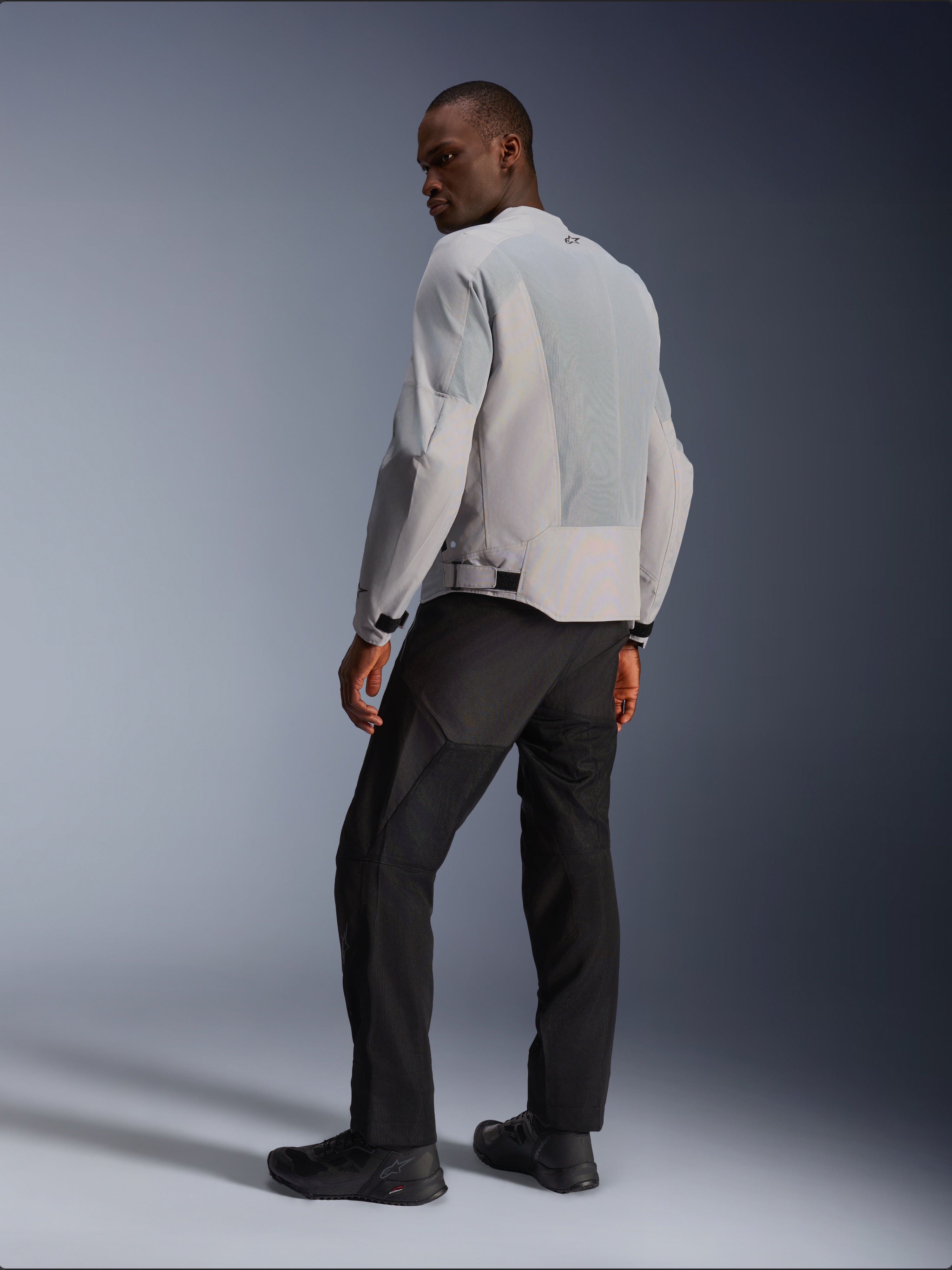 Alpinestars C-1 Air Jacket, zilver en grijs, van achteren bekeken op een model, voorzien van geventileerde tech mesh-panelen en reflecterende logo's, gedragen met een zwarte broek en schoenen, urban contemporary motorkleding.
