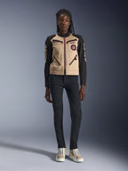 Alpinestars Stella Grace damesmotorjas, stedelijke motorjas, beige en zwarte textielconstructie, voorzien van ritsen aan de voorzijde en geborduurde Oscar-spiraalpatch, gedragen met een zwarte broek en hoge sneakers, eigentijdse op werkkleding geïnspireerde motoruitrusting