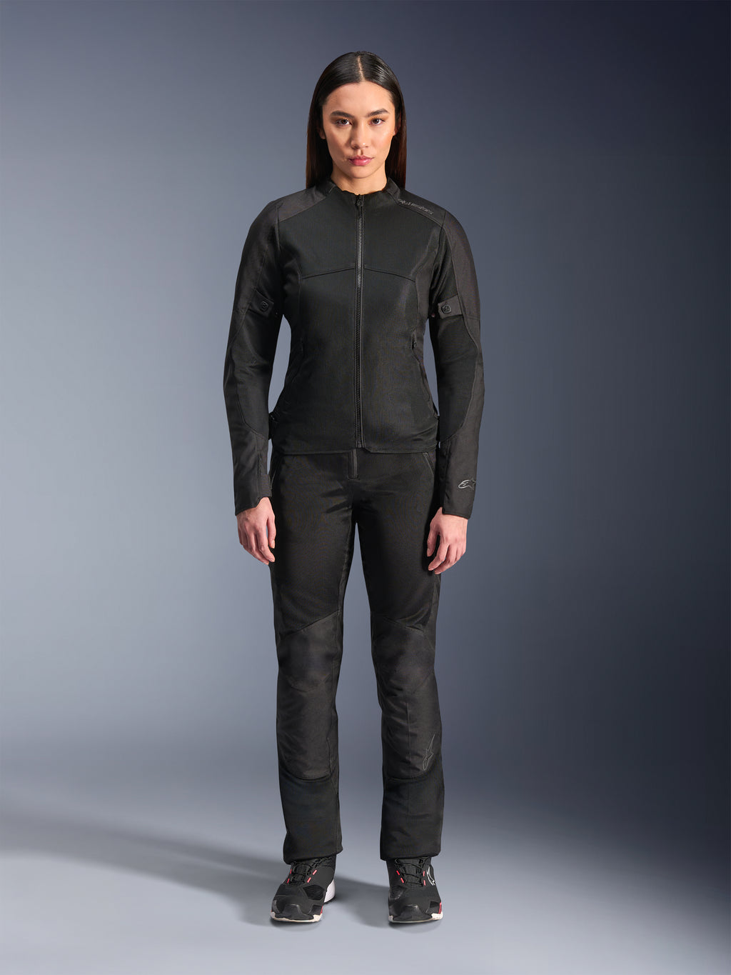 Vrouw in Alpinestars Stella C-1 Air Jas in het zwart, gecombineerd met bijpassende zwarte textiel motorbroek en motorschoenen, strak urban design met grote mesh-panelen voor optimale luchtstroom.