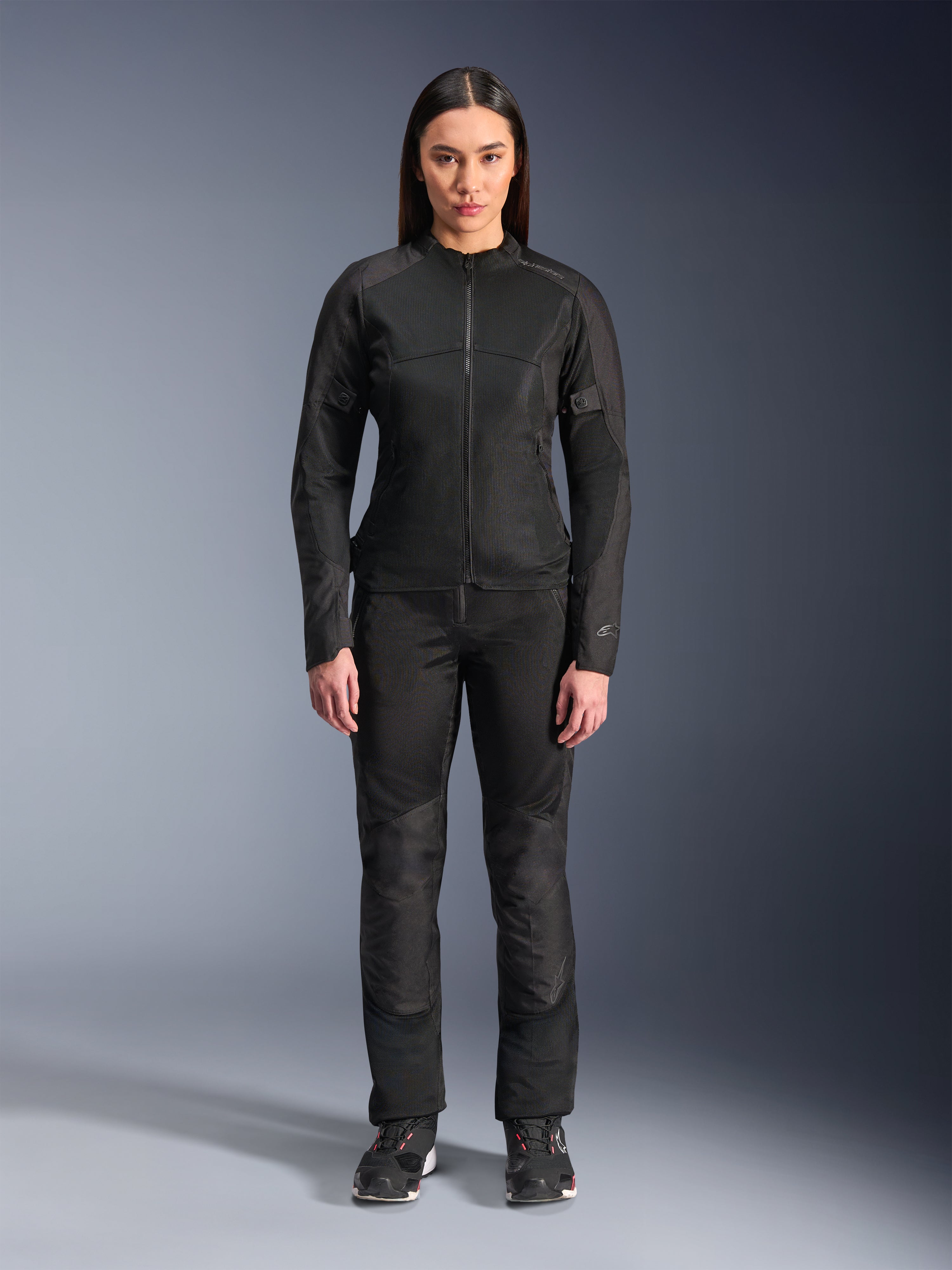 Vrouw in Alpinestars Stella C-1 Air Jas in het zwart, gecombineerd met bijpassende zwarte textiel motorbroek en motorschoenen, strak urban design met grote mesh-panelen voor optimale luchtstroom.