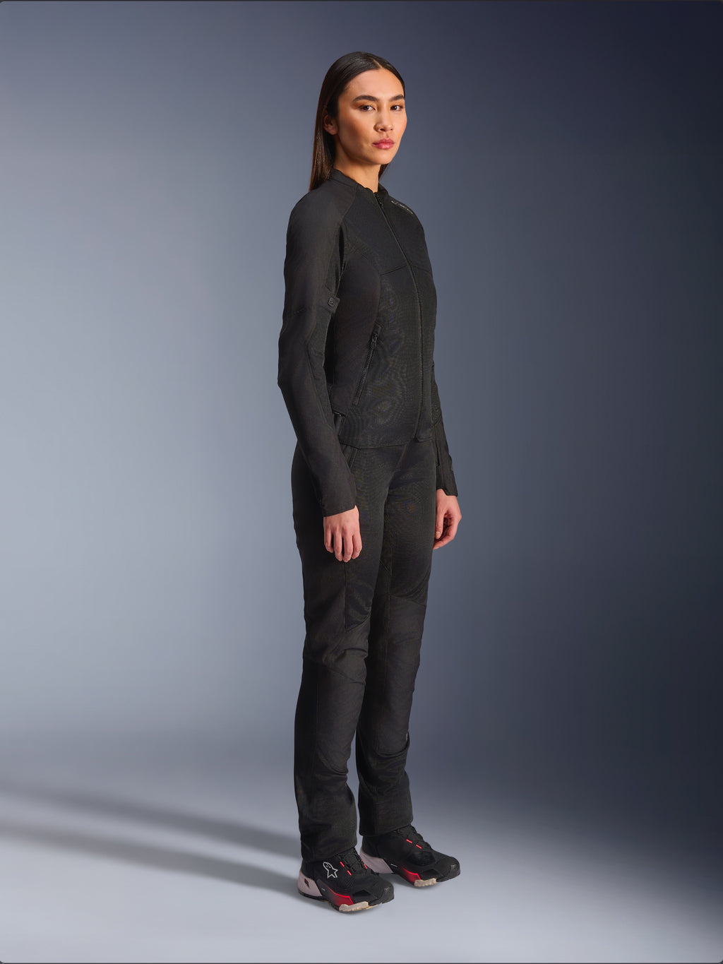 Alpinestars Stella C-1 Air damesmotorjas in het zwart, textiele motorjas met mesh panelen, gedragen met bijpassende zwarte motorbroek en technische sneakers, studio-opname van een volledige urban motoroutfit.