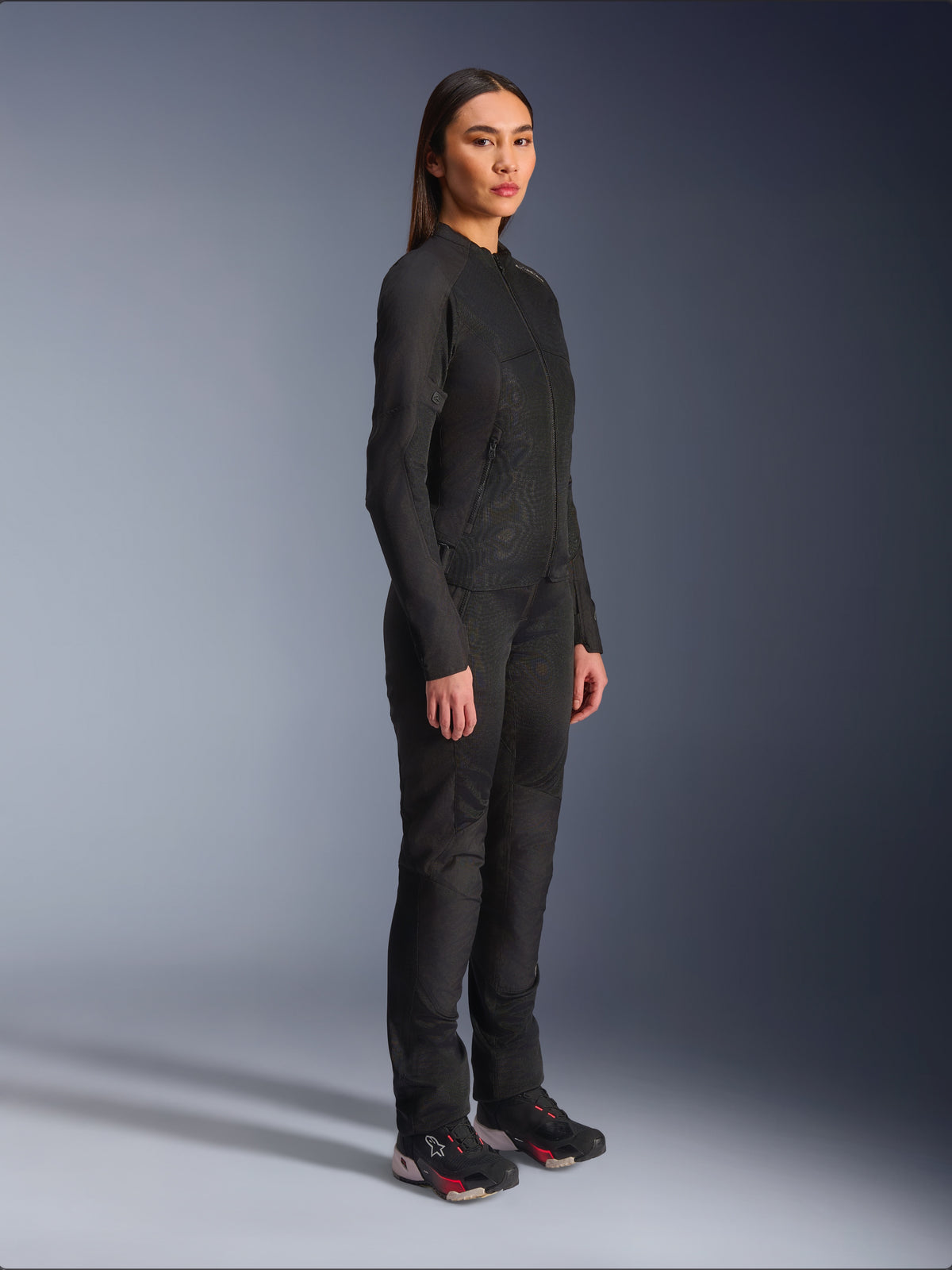Alpinestars Stella C-1 Air damesmotorjas in het zwart, textiele motorjas met mesh panelen, gedragen met bijpassende zwarte motorbroek en technische sneakers, studio-opname van een volledige urban motoroutfit.
