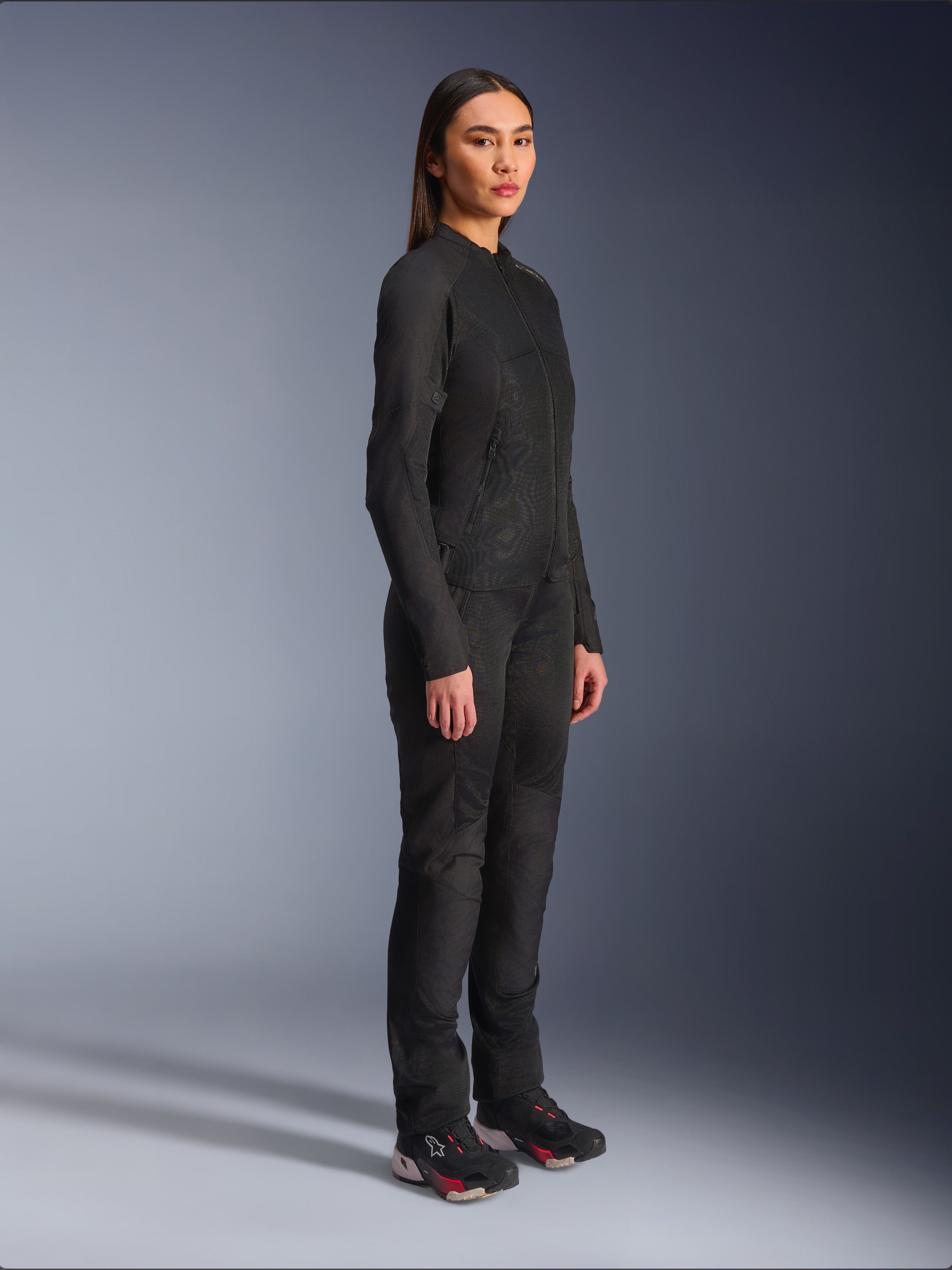 Alpinestars Stella C-1 Air damesmotorjas in het zwart, textiele motorjas met mesh panelen, gedragen met bijpassende zwarte motorbroek en technische sneakers, studio-opname van een volledige urban motoroutfit.
