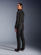 Vrouw draagt Alpinestars Stella C-1 Air Jacket in zwart, urbane textiele motorjas met mesh-panelen, achteraanzicht van opzij met de slanke pasvorm en het logo op de bovenrug, gedragen met bijpassende zwarte broek en sportschoenen, eigentijdse motoruitrusting