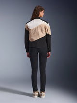 Alpinestars Stella Moshell Jacket, dames urban motorjas, achteraanzicht, asymmetrisch ontwerp in Black Sand en Off White met grote grafische omtrek, gedragen met zwarte slim-fit broek en beige sneakers, urban motoruitrusting