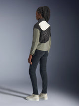 Vrouw in Alpinestars Stella Moshell Jacket, urban motorjas, zwarte, grijze en gebroken witte kleurstelling, achteraanzicht met asymmetrisch paneelontwerp en grote graphic op de rug, gecombineerd met een zwarte slim-fit broek en gebroken witte sneakers, eigentijdse urban motoruitrusting