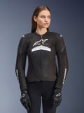 Alpinestars Stella T-GP Plus R V4 Airflow motorjas, dames motorracejas, zwart met witte en grijze accenten, getextureerd mesh-ontwerp, logo op de borst en mouwen, gedragen met bijpassende zwart-witte handschoenen