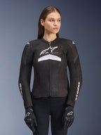 Alpinestars Stella T-GP Plus R V4 Airflow motorjas, dames motorracejas, zwart met witte en grijze accenten, getextureerd mesh-ontwerp, logo op de borst en mouwen, gedragen met bijpassende zwart-witte handschoenen