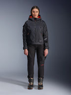 Vrouwelijk model draagt de Alpinestars Molly Air Jacket in Black en Fluo Coral, voorzien van een op utility geïnspireerd ontwerp met een capuchon en koraalrode binnenvoering, gecombineerd met een zwarte motorbroek en motorlaarzen, urban contemporary motoruitrusting