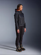 Vrouwelijke motorrijder met de Alpinestars Molly Air motorjas in Black Fluo Coral, lichtgewicht textiele motorjas met een feloranje capuchonvoering, gecombineerd met een zwarte motorbroek en technische laarzen, urban contemporary utility-geïnspireerd ontwerp.