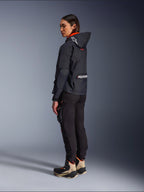 Vrouwelijke motorrijder in de Alpinestars Molly Air Jacket in Black Fluo Coral, achteraanzicht van de zijkant toont de capuchon met Astars-logo en grote Alpinestars-branding op de rug, gecombineerd met een zwarte cargo motorbroek en beige met zwarte adventure laarzen, eigentijdse stedelijke motoruitrusting voor dames