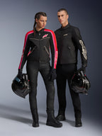 Man en vrouw poserend in Alpinestars motoruitrusting, man draagt het zwarte T-Dyno Air Jacket, vrouw draagt een zwarte textieljas met roze en rode accenten, beiden houden zwarte integraalhelmen vast, gestyled met zwarte motorbroeken en laarzen.