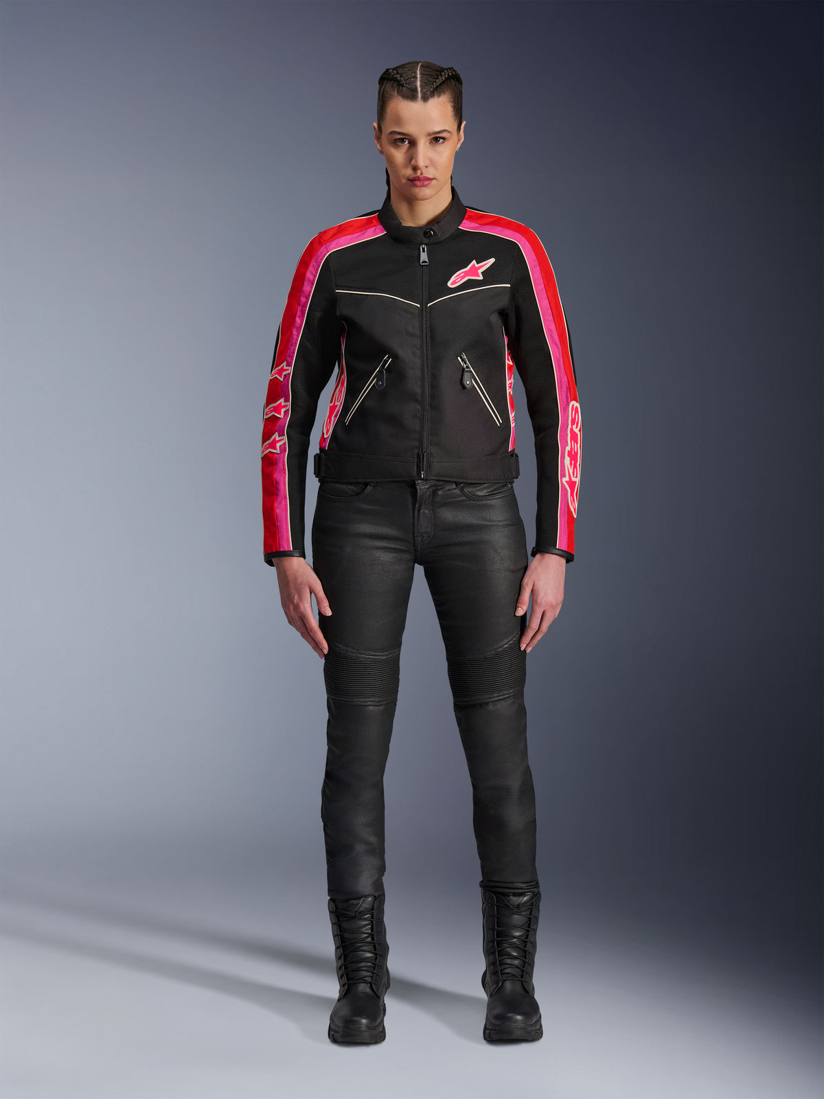 Vrouwelijke rijder draagt de Alpinestars Stella T-Dyno Air jas, zwart met felrode en fuchsia accenten, gecombineerd met een zwarte motorbroek en veterlaarzen, voorzien van 3D-meshpanelen, een getailleerde pasvorm en roze sterlogo's, urban motoruitrusting