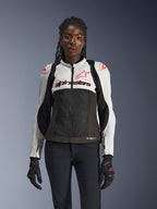 Alpinestars Woman Stella SMX Air Jacket, Ice Gray, Black, and Coral Fluo, featuring mesh construction and perforated panels, worn by a female model with black motorcycle gloves and pants, front view.