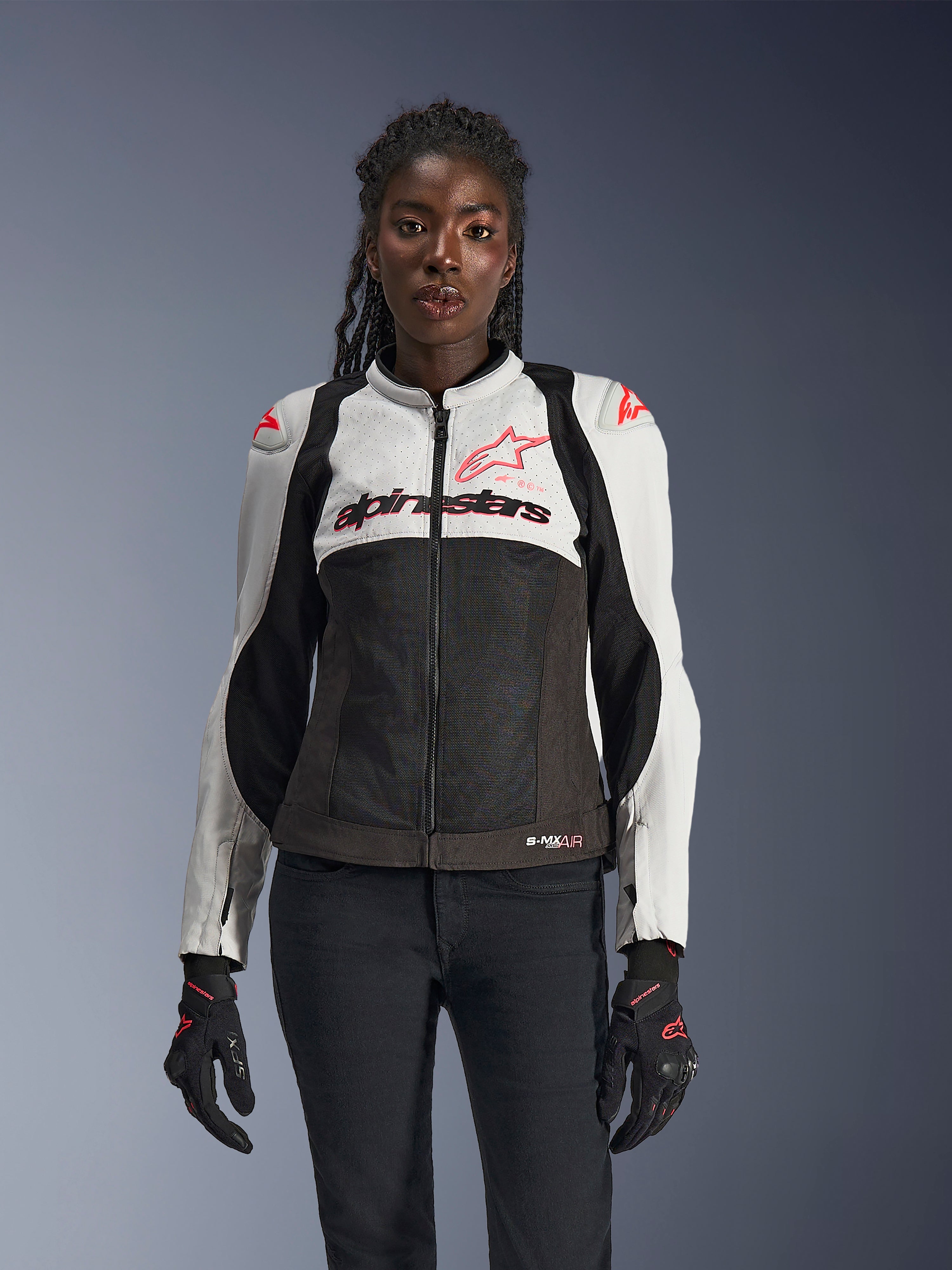 Alpinestars Stella SMX Air motorjas voor dames, Ice Gray, zwart en Coral Fluo, voorzien van mesh-constructie en geperforeerde panelen, gedragen door een vrouwelijk model met zwarte motorhandschoenen en broek, vooraanzicht.