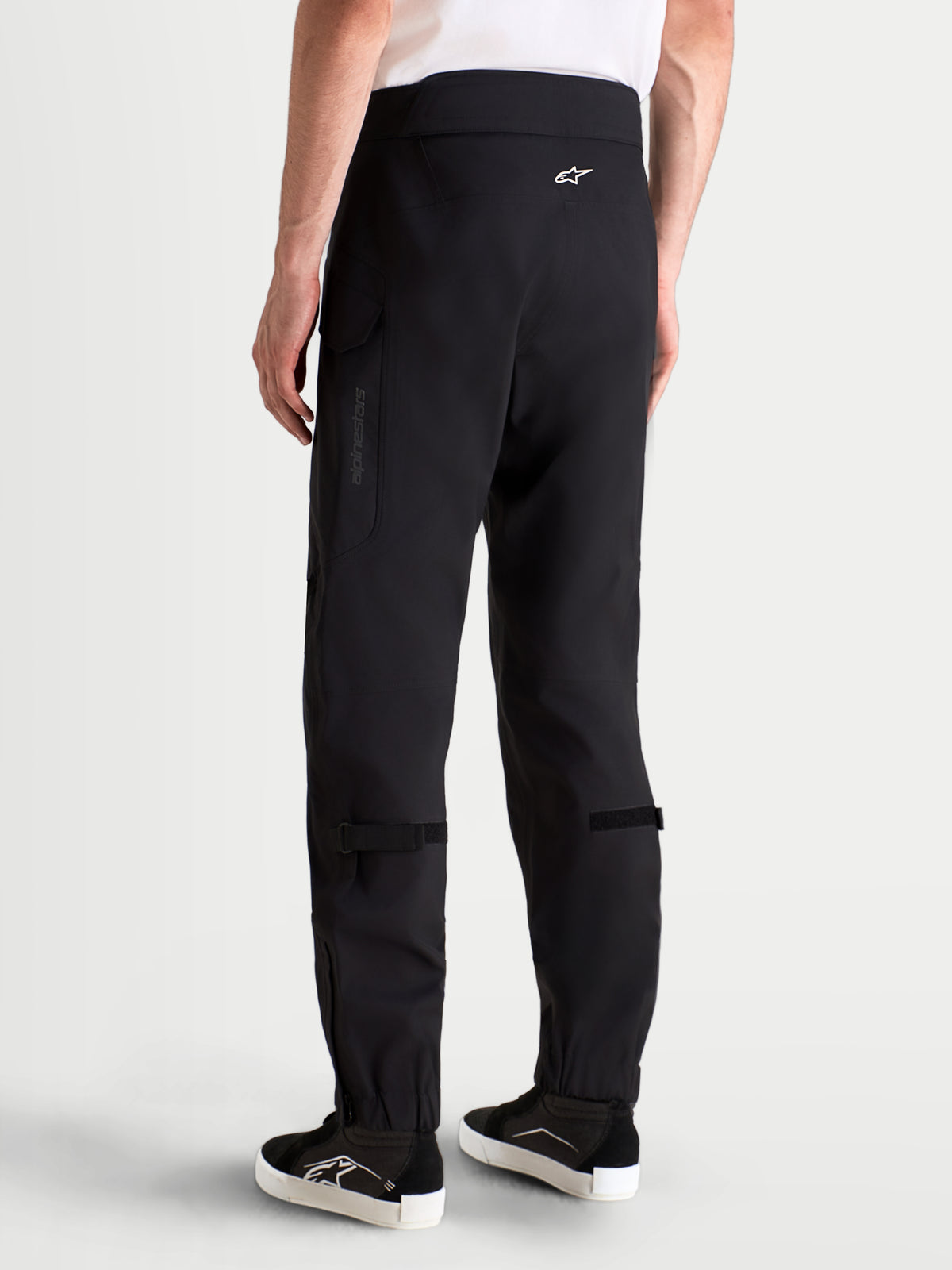 Alpinestars Juggernaut V2 Drystar broek, waterdichte urban motorbroek voor heren in zwart, achteraanzicht op model met bijpassende uitrusting en laarzen, met hoge tailleband en cargozakken