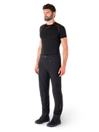 Alpinestars Alden broek, urban motorbroek, zwart, regular fit softshell textiel, gedragen door een model met een zwarte basislaag en rijschoenen, voorzien van een tailleband met magnetische sluiting en zakken met ritssluiting