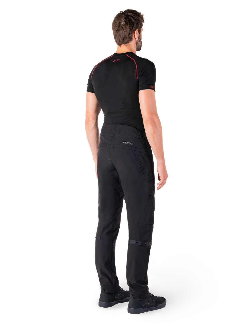 Alpinestars Alden broek, zwarte urban motorbroek, achteraanzicht op een model, gedragen met zwarte basislaag met korte mouwen en zwarte motorschoenen, voorzien van gewatteerde details en reflecterende MO.ST.EQ. branding op de achterpas