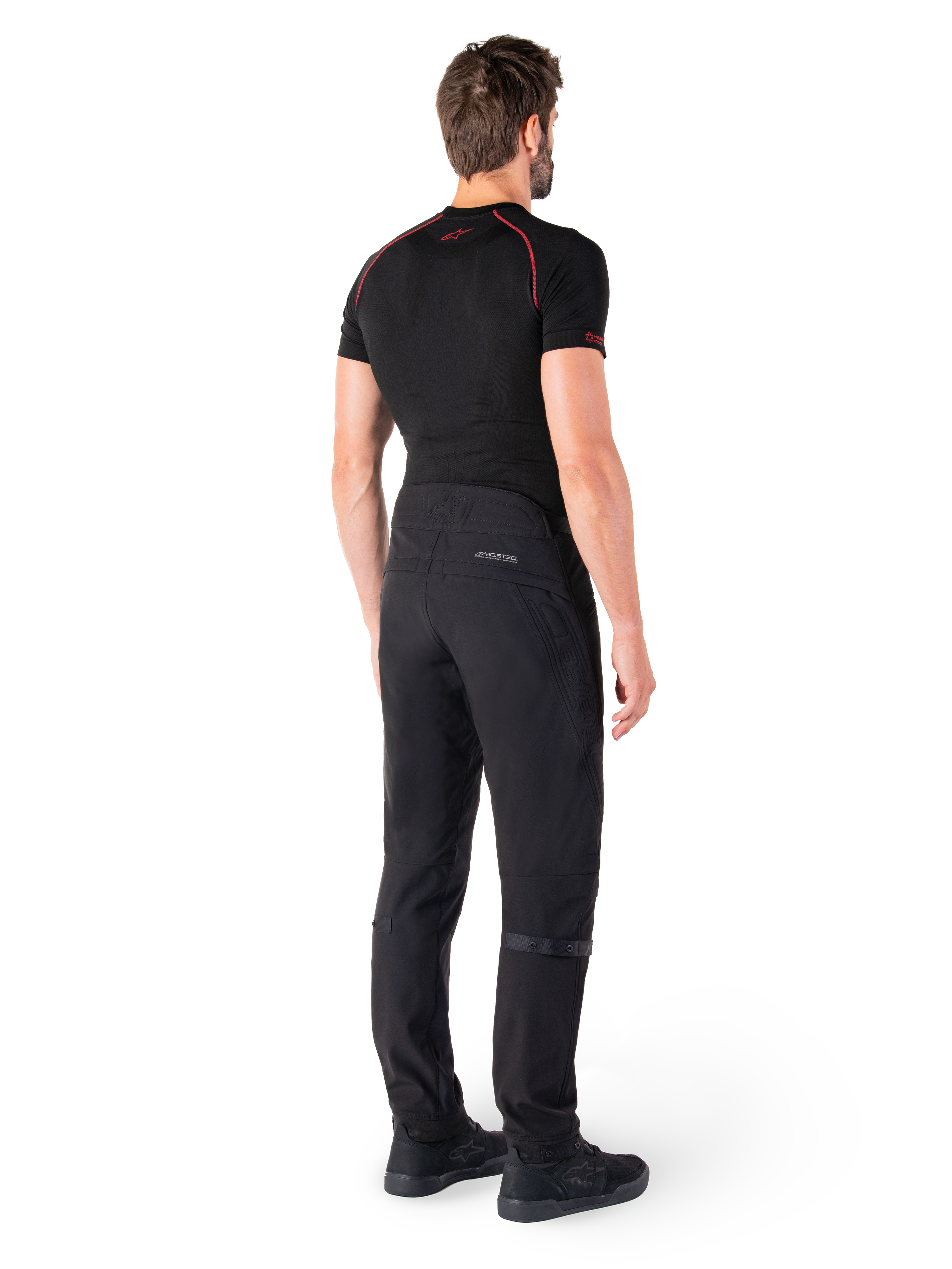 Alpinestars Alden broek, zwarte urban motorbroek, achteraanzicht op een model, gedragen met zwarte basislaag met korte mouwen en zwarte motorschoenen, voorzien van gewatteerde details en reflecterende MO.ST.EQ. branding op de achterpas