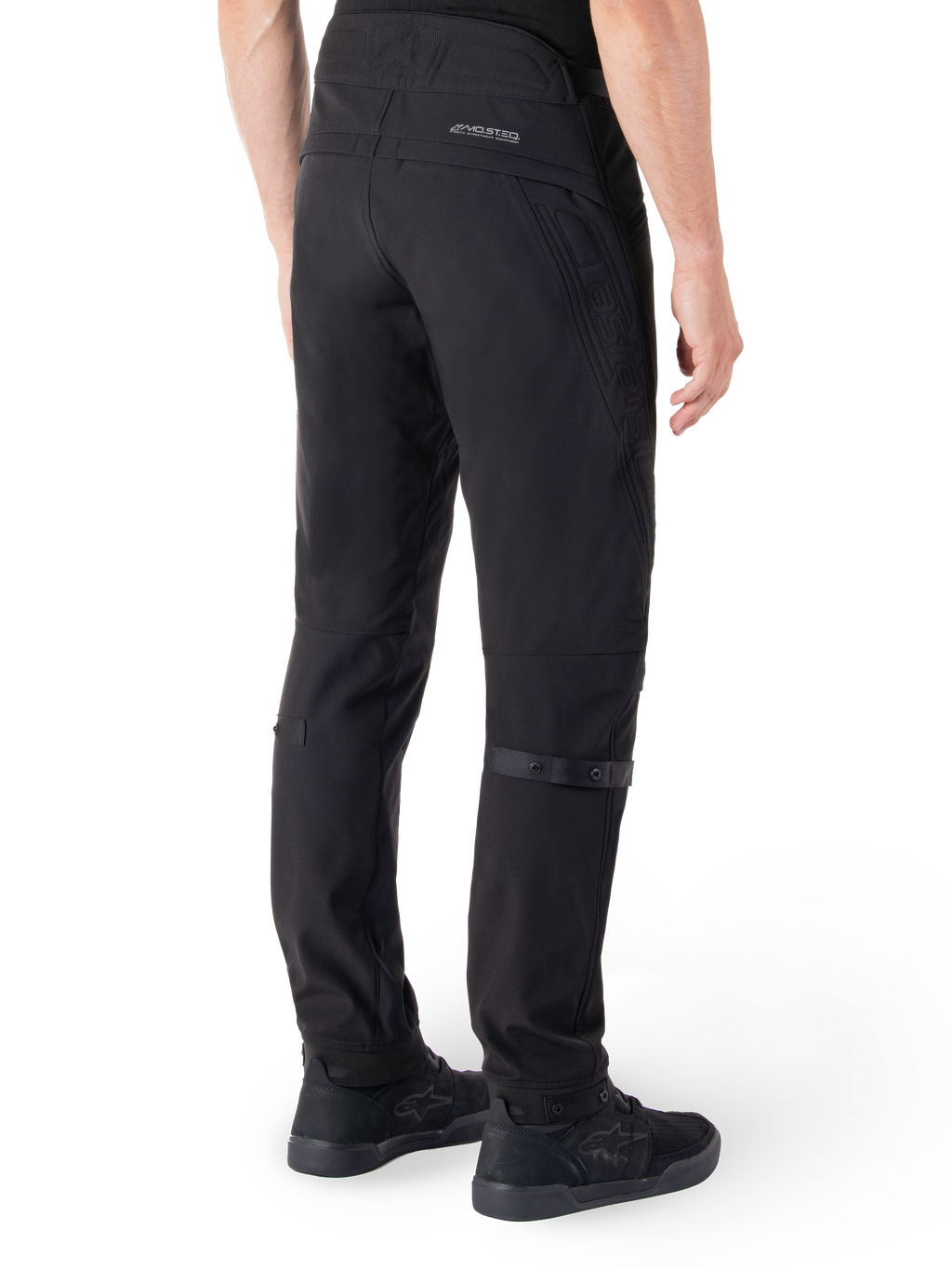 Alpinestars Alden broek, urban motorbroek, zwart, achteraanzicht met technische softshell stof en gewatteerde details, MO.ST.EQ. reflecterende branding op de achterpas en verstelbare kuitbanden, gecombineerd met zwarte motorschoenen