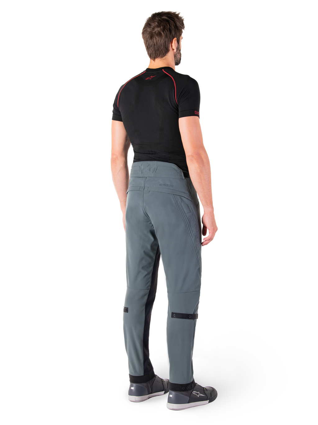 Alpinestars Alden broek, Urban Gray, achteraanzicht, technische textiele motorbroek met gewatteerde details op de achterzijde van de taille en de benen, gecombineerd met een zwarte basislaag en grijze motorschoenen, eigentijdse urban streetwear-stijl.