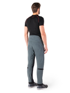 Alpinestars Alden broek, Urban Gray, achteraanzicht, technische textiele motorbroek met gewatteerde details op de achterzijde van de taille en de benen, gecombineerd met een zwarte basislaag en grijze motorschoenen, eigentijdse urban streetwear-stijl.