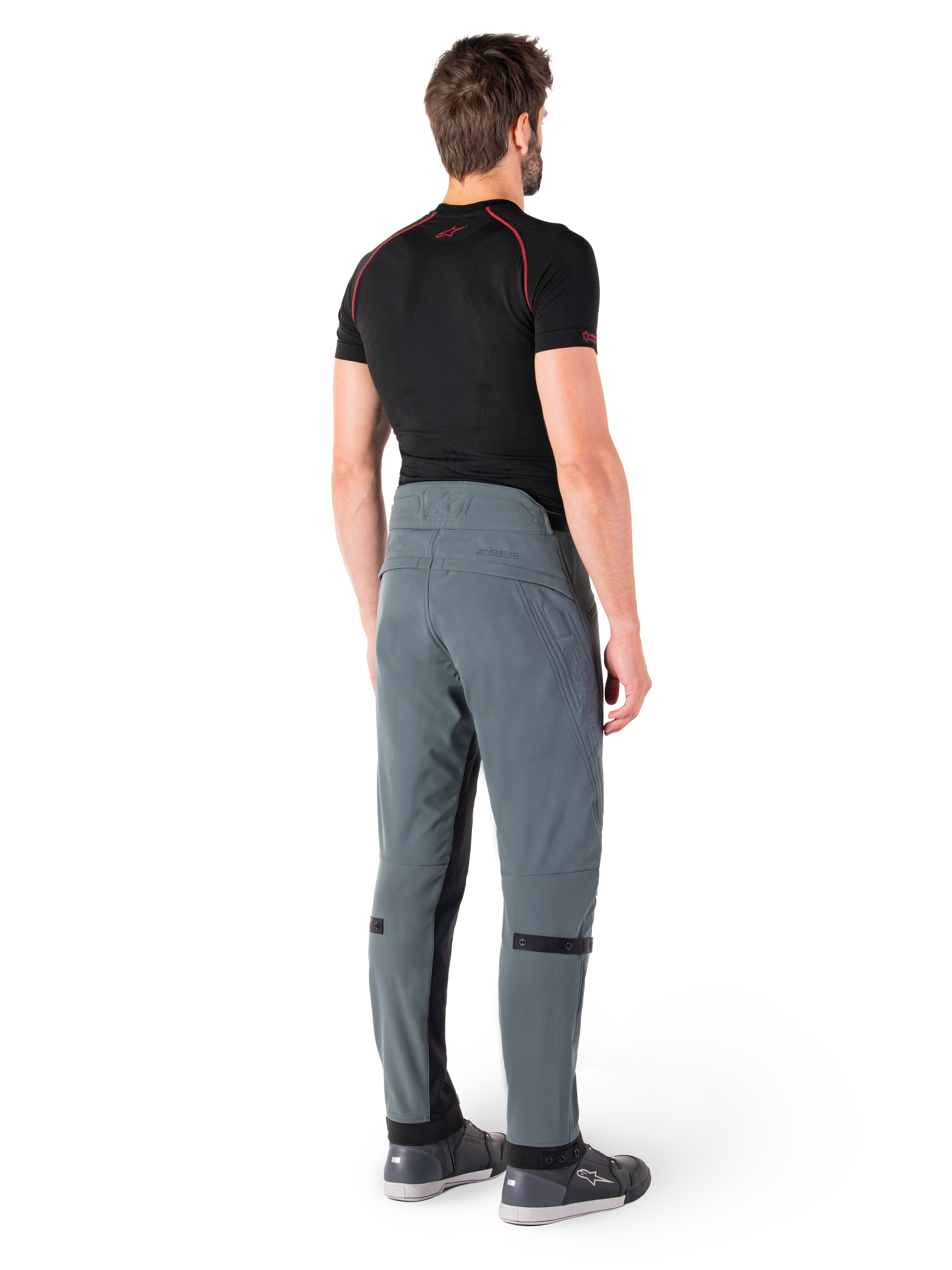 Alpinestars Alden broek, Urban Gray, achteraanzicht, technische textiele motorbroek met gewatteerde details op de achterzijde van de taille en de benen, gecombineerd met een zwarte basislaag en grijze motorschoenen, eigentijdse urban streetwear-stijl.