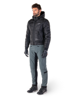 Alpinestars Alden broek in Urban Gray, gedragen door een model met een zwart gewatteerd jack met capuchon, handschoenen en rijschoenen, voorzien van gewatteerde details aan de zijkanten en zwarte binnenbeenpanelen, streetwear-geïnspireerde stedelijke motoruitrusting.