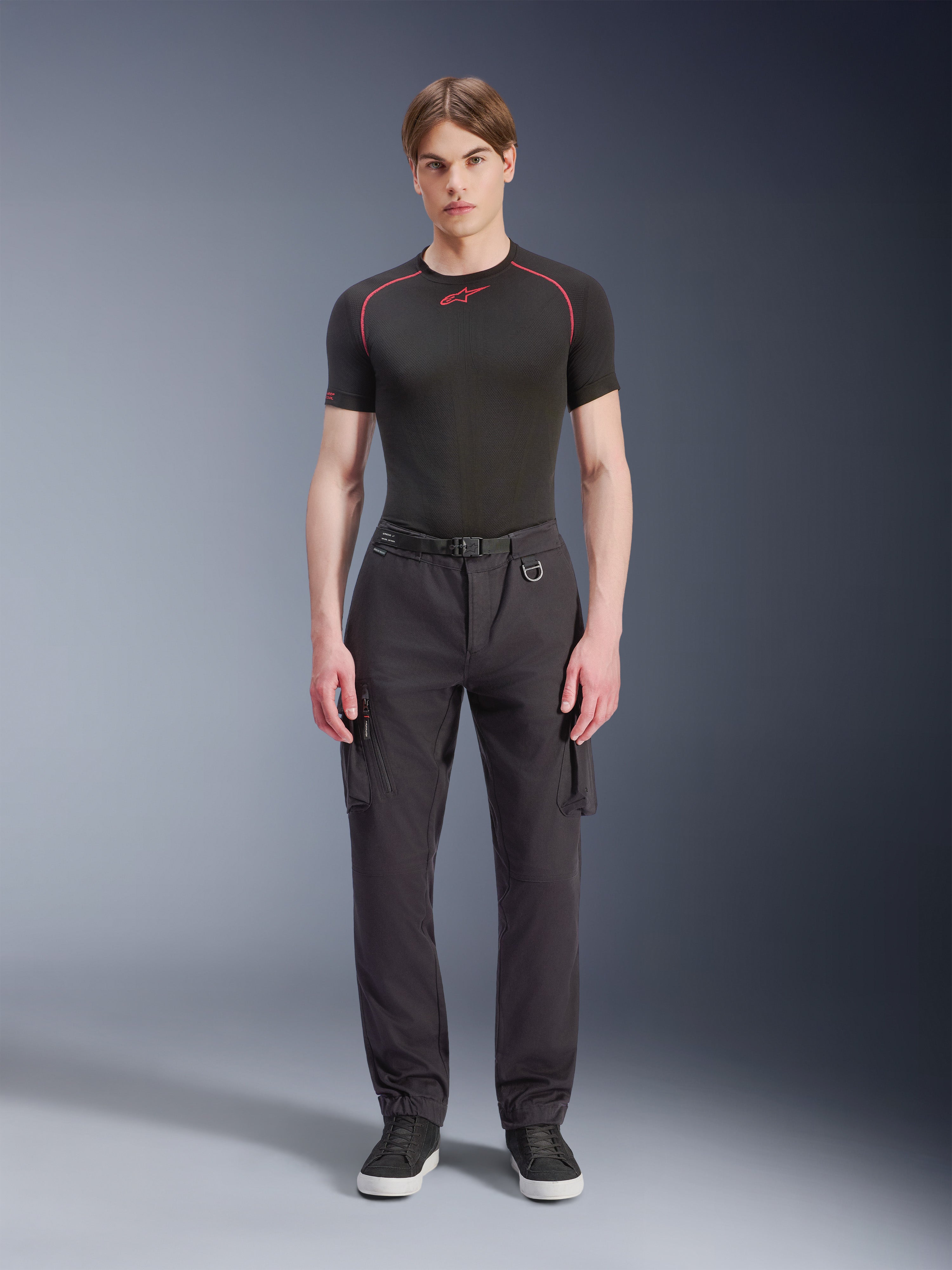 Alpinestars Flex-AST Cargo Pants, Black, urban motorcycle pants worn by a male model with a black short-sleeved top and sneakers, featuring a regular tapered fit, cargo pockets, and integrated belt buckle detail
