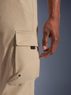Alpinestars Flex-AST Cargo Pants, Light Beige, close-up of the side cargo pocket featuring an embroidered star logo on the flap, metal eyelet detail, and black herringbone tape accent, urban motorcycle riding pants.