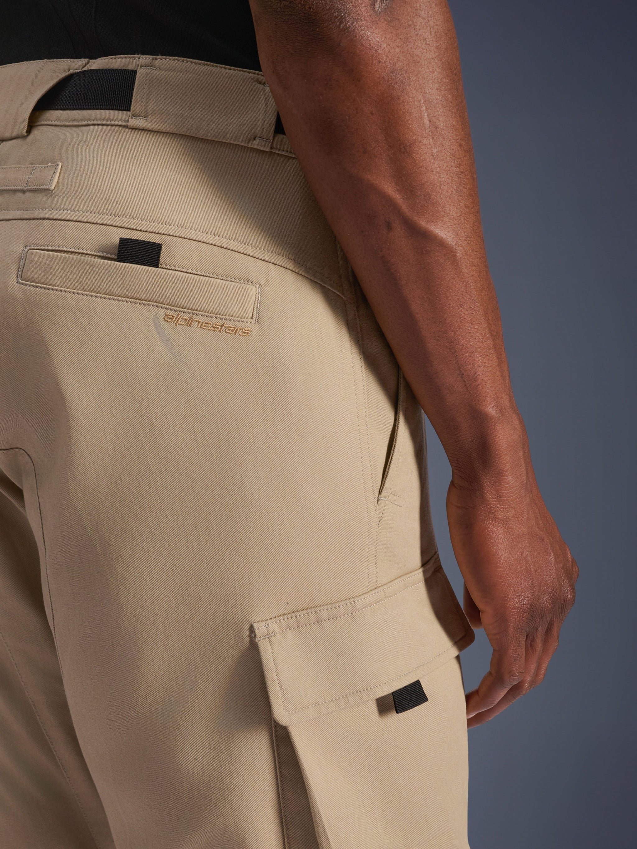 Alpinestars Flex-AST Cargo Pants - Short, Light Beige, close-up side view showing cargo pocket with black pull tab and embroidered logo on rear pocket, durable textile material, urban motorcycle gear.
