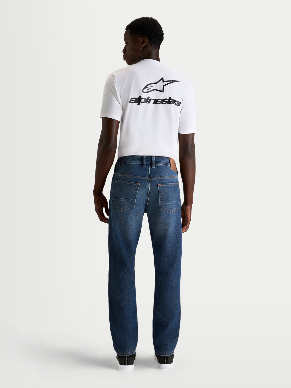 Alpinestars Flex-AST 8 Denim Pants Short, men's urban motorcycle riding jeans in medium blue, rear profile view on a model wearing a white t-shirt, AA-certified protective single-layer denim with stretch comfort.