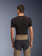 Alpinestars Flex-AST Explorer broek, achteraanzicht op model, Walnut Black, voorzien van tan textiel met versterkte zwarte zitpanelen en een elastische tailleband, gecombineerd met een zwarte basislaag met korte mouwen en rode stiksels