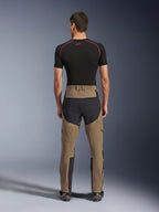 Alpinestars Flex-AST Explorer broek, Walnut Black, achteraanzicht op model, met versterkt zwart zitvlak en bruin stretchtextiel, gecombineerd met een zwarte base layer en technische motorlaarzen, duurzame adventure motorkleding